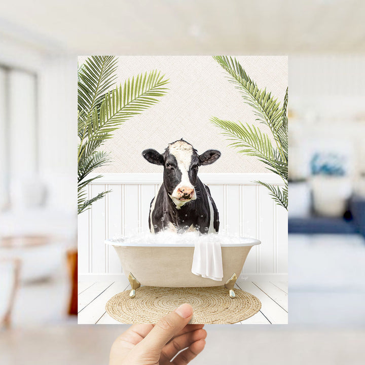 A black and white cow is sitting in a bathtub filled with water, surrounded by green palm leaves, creating a whimsical and playful scene.