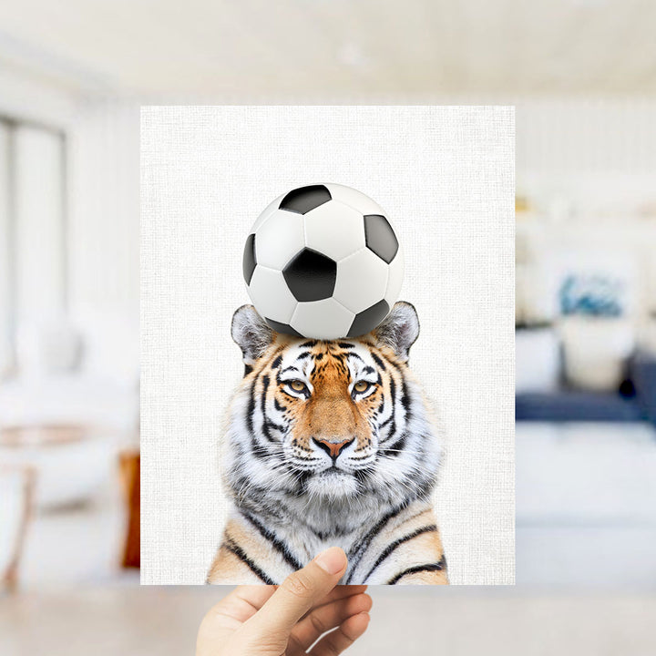 A tiger is standing on a soccer ball, with the ball placed on its head.