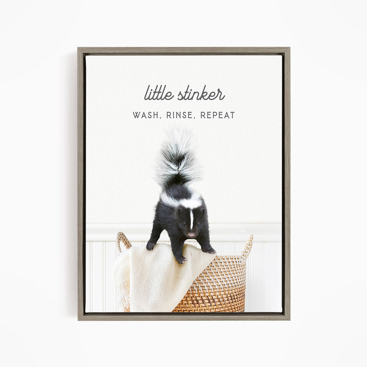 A black and white skunk standing on a woven basket, with the text "little stinker" and "WASH, RINSE, REPEAT" written above it.