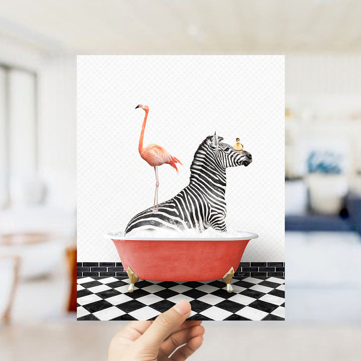 A hand holds up a framed image depicting a zebra sitting in a red bathtub, with a pink flamingo standing on its back.