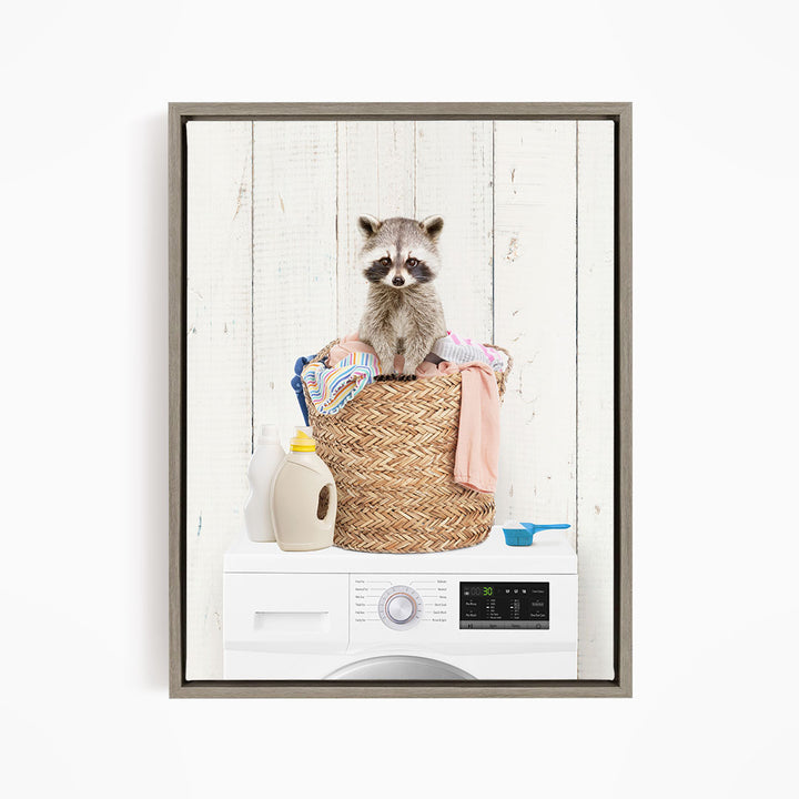 A raccoon sitting in a woven laundry basket filled with clothes and laundry supplies, including a detergent bottle and a measuring cup.