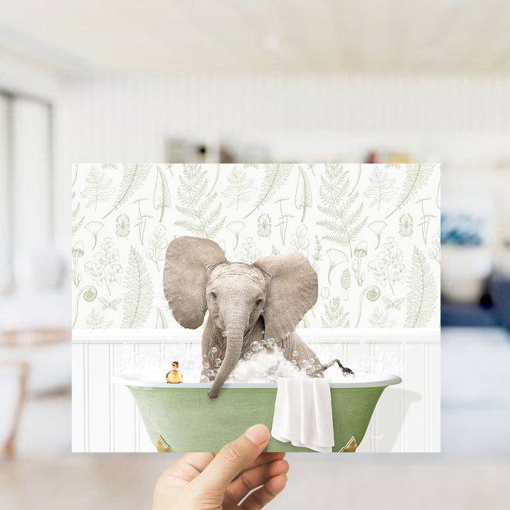 A hand holds up a collage of two images: one of an elephant sitting in a bathtub and another of a person sitting in the same bathtub.