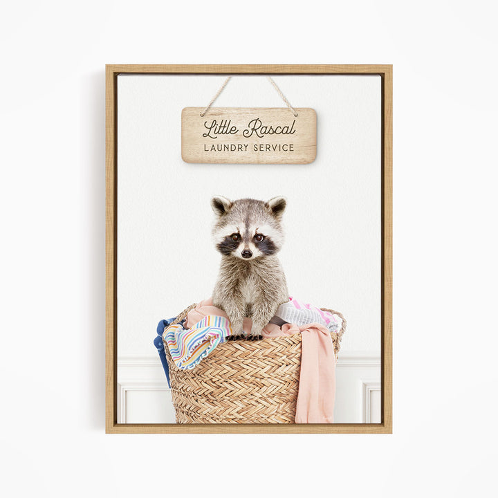 A raccoon sitting in a woven laundry basket, with a wooden sign above it that reads "Little Racal Laundry Service".