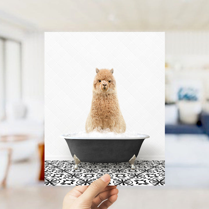 A fluffy brown alpaca sitting in a black bathtub filled with bubbles, with a hand holding the image up to the viewer.
