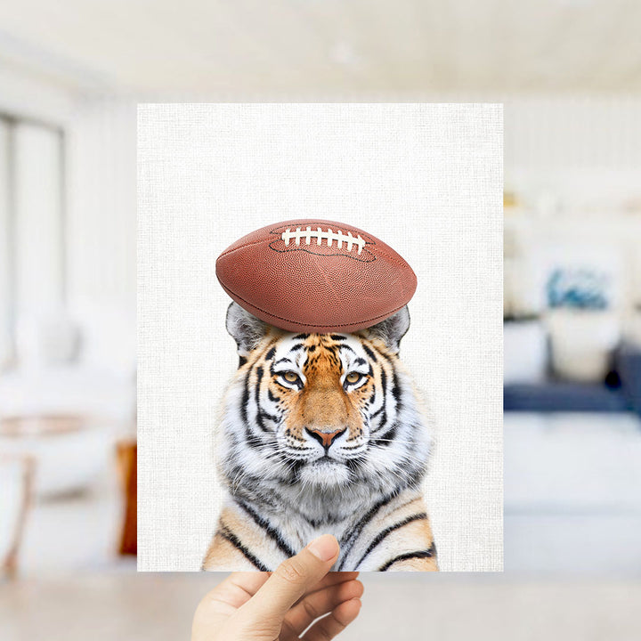 A tiger wearing a football helmet is being held up against a white background.