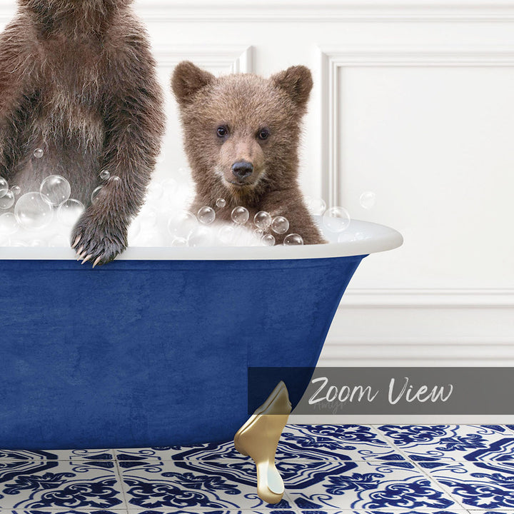 A baby bear sitting in a blue bathtub filled with bubbles, with another bear standing on the edge of the tub.