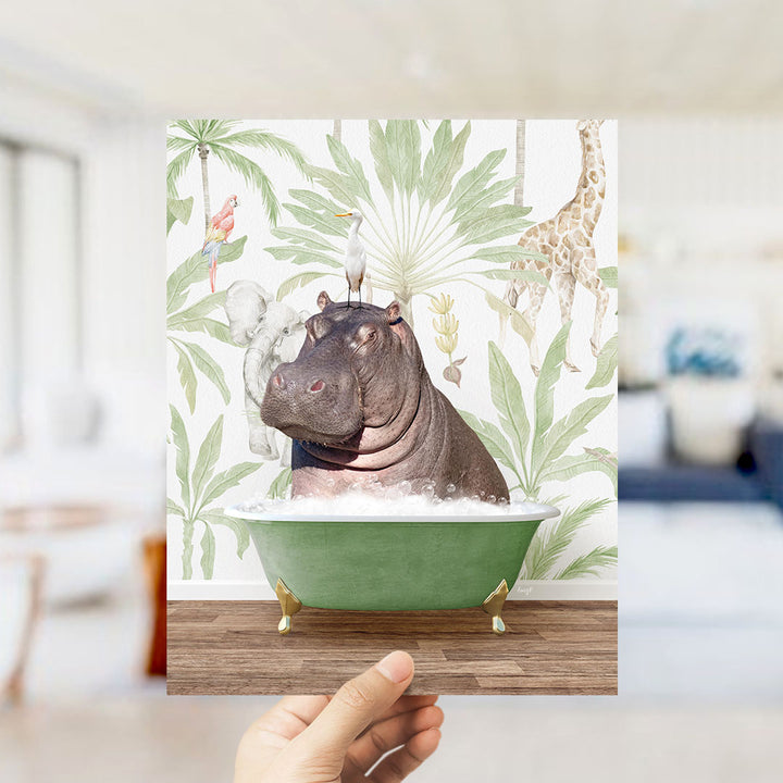 A hand holds up a framed image depicting a hippopotamus sitting in a green bathtub, surrounded by tropical foliage and animals.