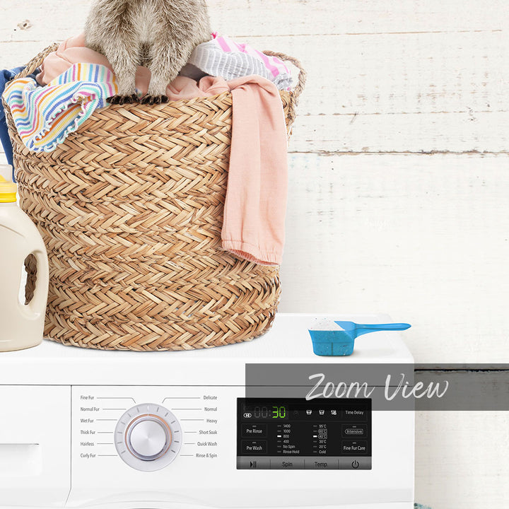 A laundry basket filled with clothes sits on top of a washing machine, with a blue measuring cup and a white bottle nearby.