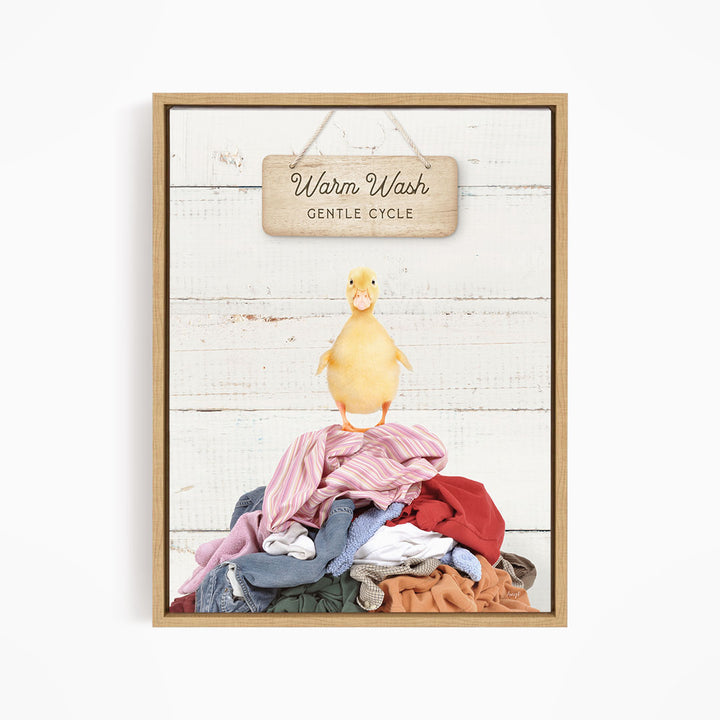 A yellow duck standing on a pile of clothes, with a wooden sign above that says "Warm Wash Gentle Cycle".