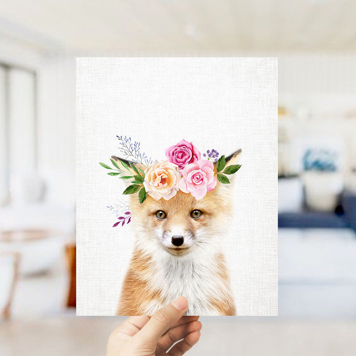 A hand is holding up a framed print of a fox wearing a floral crown.