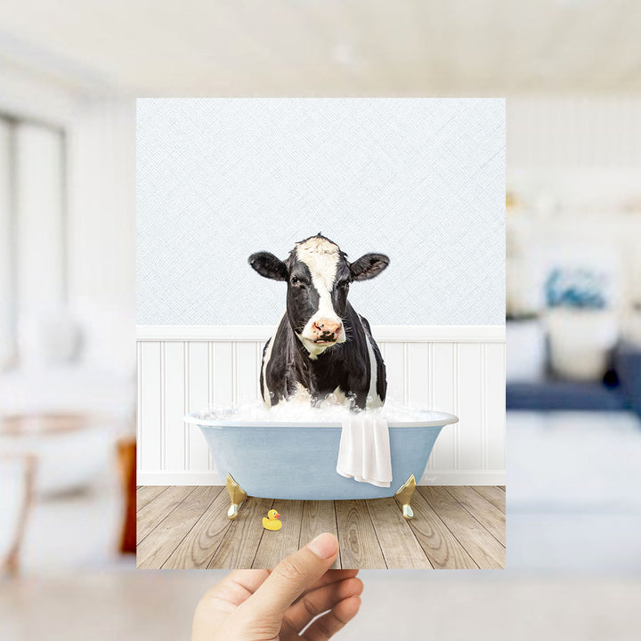 A black and white cow is sitting in a blue bathtub filled with water, with a yellow rubber duck floating nearby.