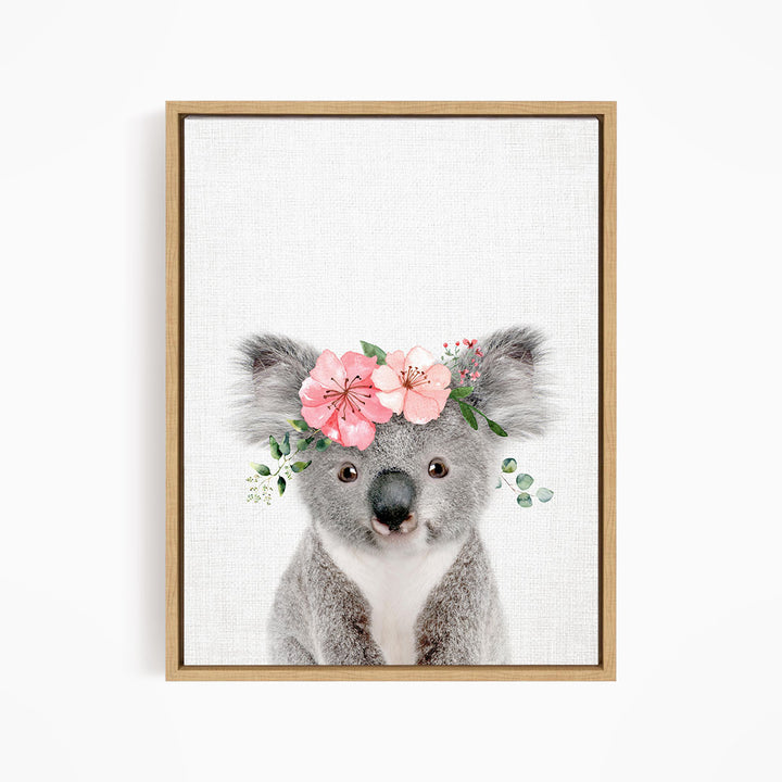 A cute koala bear wearing a floral crown of pink flowers and green leaves.
