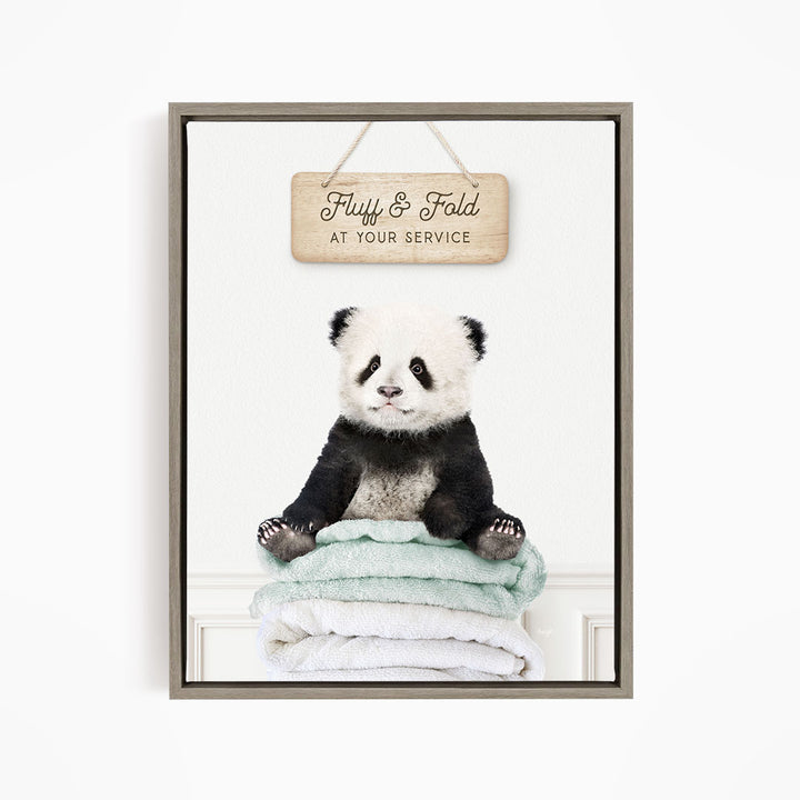 A panda bear sitting on a stack of towels, with a wooden sign above that says "Fuffy & Fold at your service".
