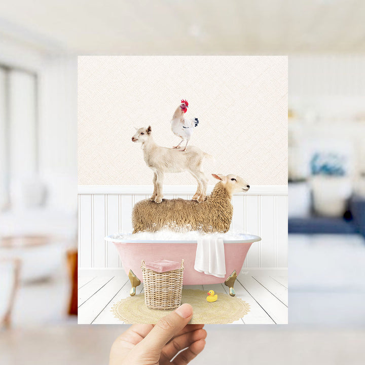 A hand holds up a framed image depicting a goat standing on a sheep's back while a chicken sits on top of a sheep in a pink bathtub.