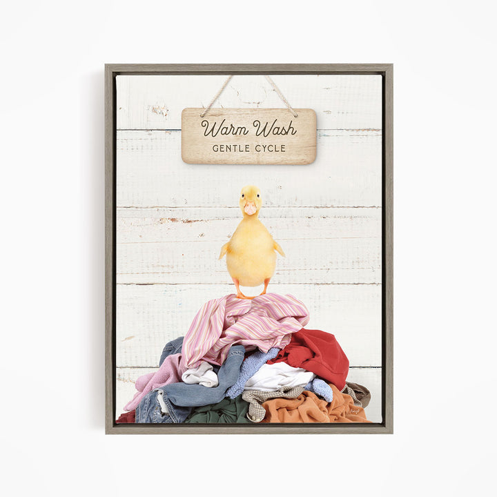 A yellow duck standing on a pile of clothes, with a wooden sign above that reads "Warm Wash Gentle Cycle".
