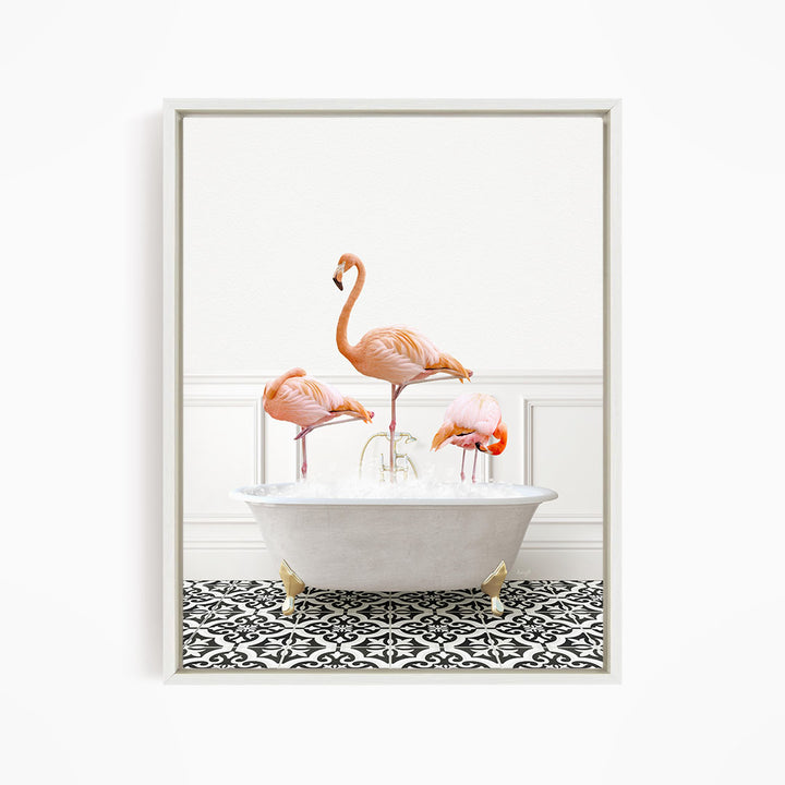 A framed image depicting three pink flamingos standing in a white bathtub filled with water, set against a white wall and black and white patterned floor.