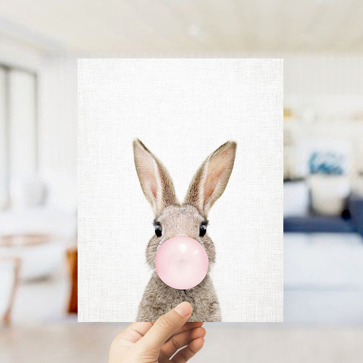 A hand is holding up a picture of a rabbit blowing a bubble with a pink bubble gum bubble.