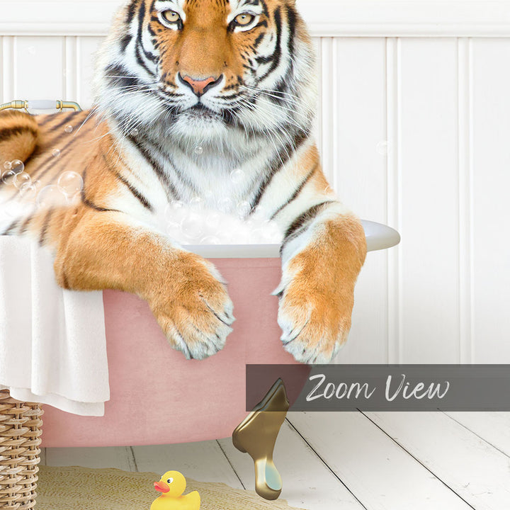A tiger is sitting in a pink bathtub filled with bubbles, surrounded by a yellow rubber duck and a white basket.
