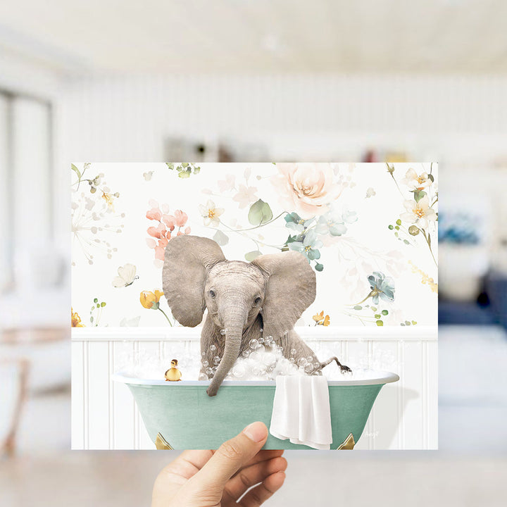 A hand holds up a collage of two images featuring an elephant sitting in a bathtub filled with water and bubbles, surrounded by a floral pattern.