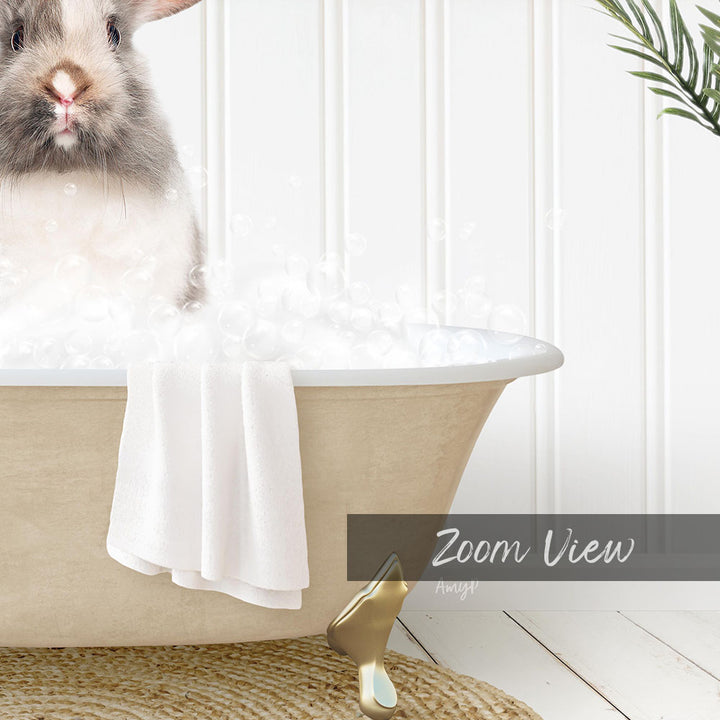 A fluffy gray and white rabbit sitting in a bathtub filled with bubbles, with a towel and gold bathtub leg visible.