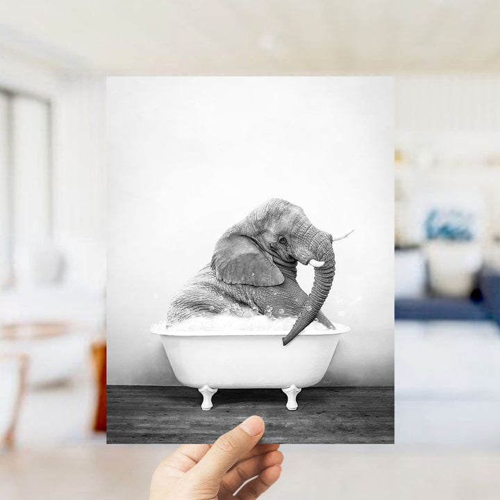 A hand holds up a black and white photograph of an elephant sitting in a bathtub filled with water.