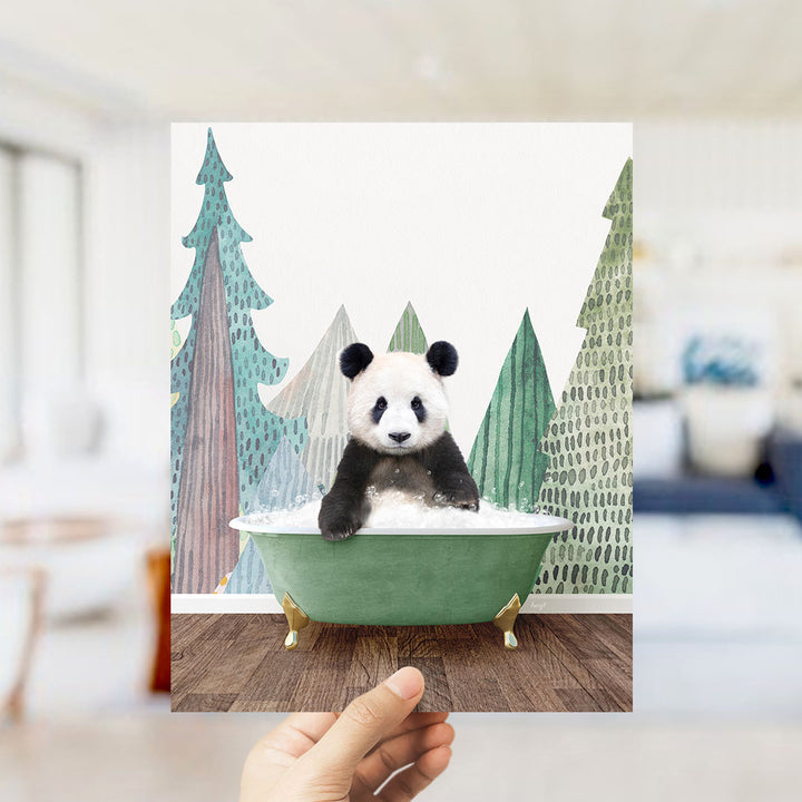 A hand holds up a framed image of a panda bear sitting in a green bathtub, surrounded by a winter landscape with trees and snow.