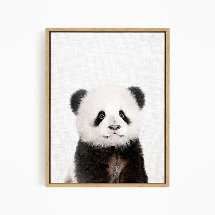 A panda bear with black and white fur is the main subject of the framed print, which is displayed on a white wall.