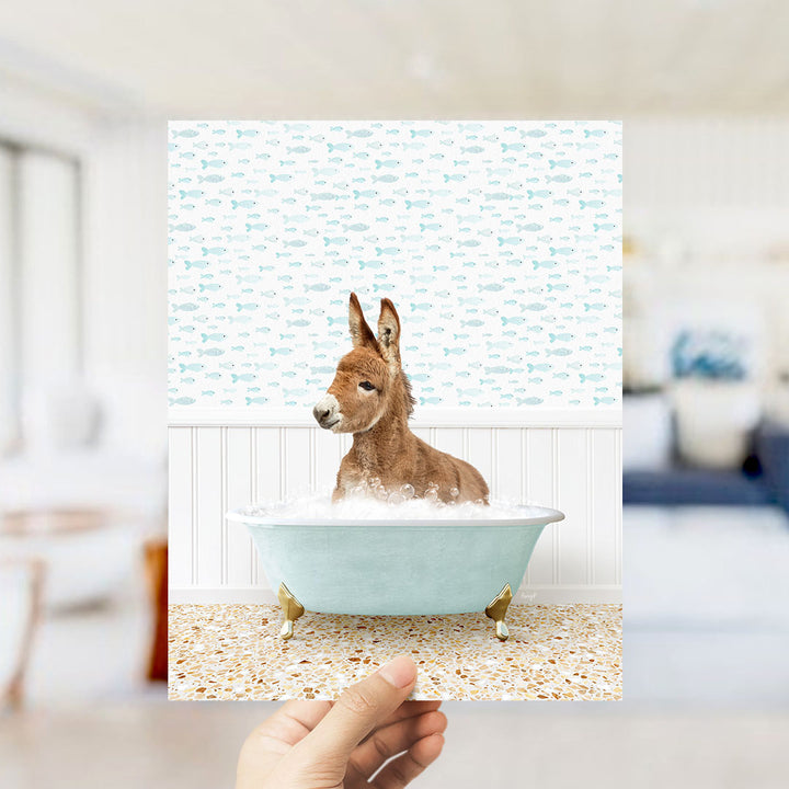 A donkey is sitting in a bathtub filled with bubbles, surrounded by a pattern of fish.