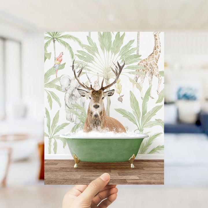 A hand holds up a framed image depicting a deer in a bathtub surrounded by tropical foliage, including a giraffe and palm trees.