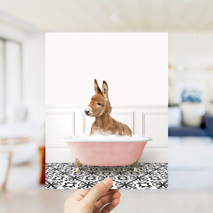 A donkey is sitting in a pink bathtub filled with bubbles, looking directly at the camera.