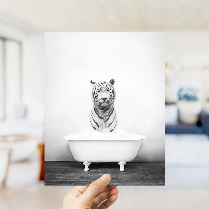 A hand holds up a framed photograph of a tiger sitting in a bathtub filled with water, creating a whimsical and playful scene.