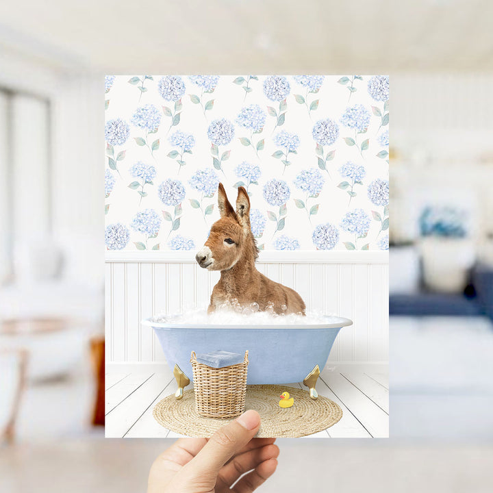 A donkey is sitting in a blue bathtub filled with bubbles, surrounded by a floral patterned wall.