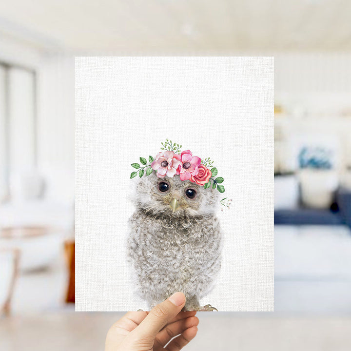 A person is holding up a framed print of a cute, fluffy owl wearing a floral headpiece.