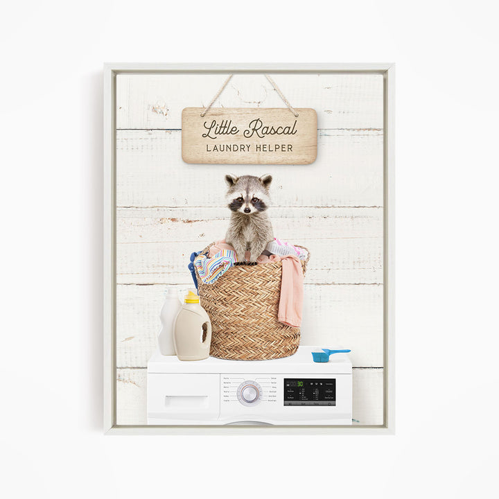 A raccoon sitting in a woven laundry basket, with a sign that reads "Little Racal Laundry Helper" above it.
