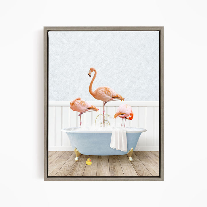A framed image depicting three flamingos standing in a bathtub filled with water, with a towel hanging on the side.