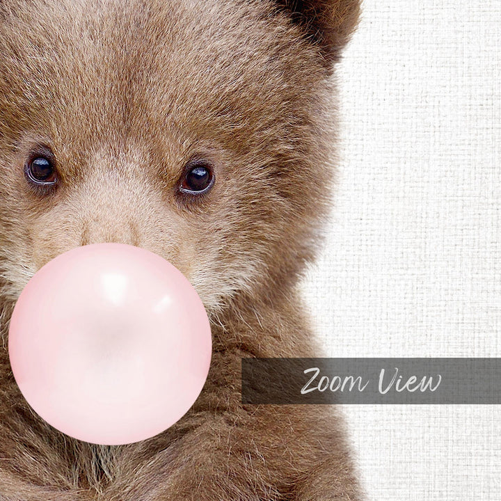 A close-up of a brown bear blowing a pink bubble with its mouth, against a white background.