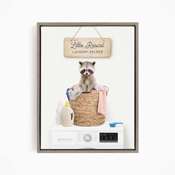 A raccoon sitting in a woven laundry basket, with a sign that reads "Little Racal Laundry Helper" above it.
