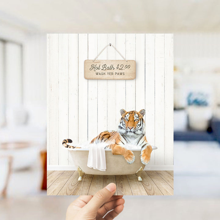 A hand holding a framed image of a tiger sitting in a bathtub, with a sign above it that says "Hot Bath $2.00 WASH YOUR Paws".