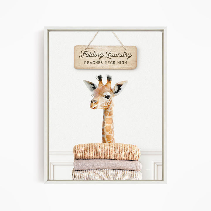 A giraffe standing on a pile of folded clothes, with a wooden sign above that says "Folding Laundry Reaches necks high".
