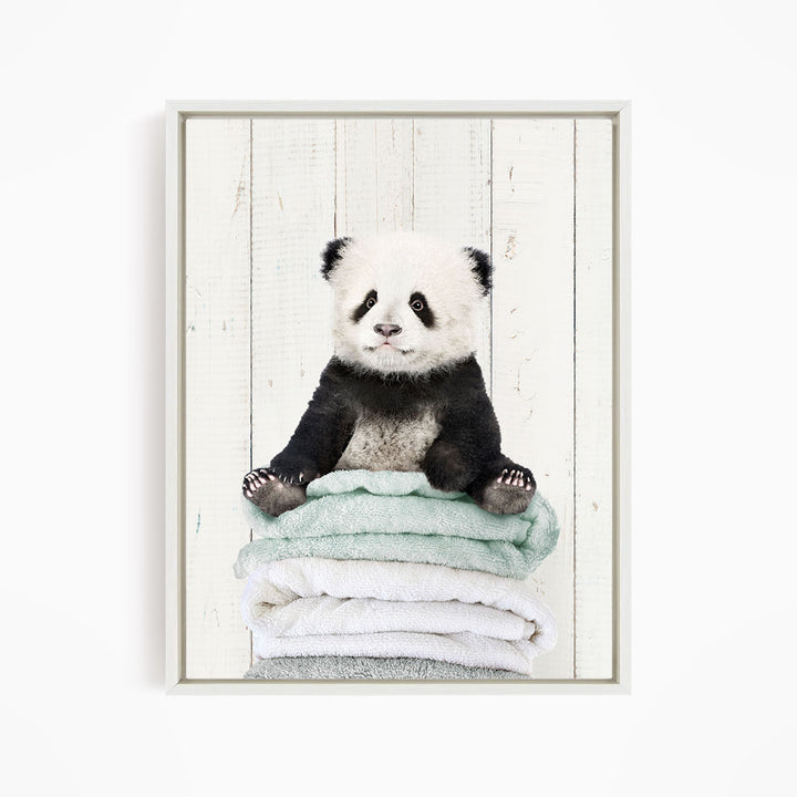 A cute panda bear sitting on a stack of towels against a white wooden background.