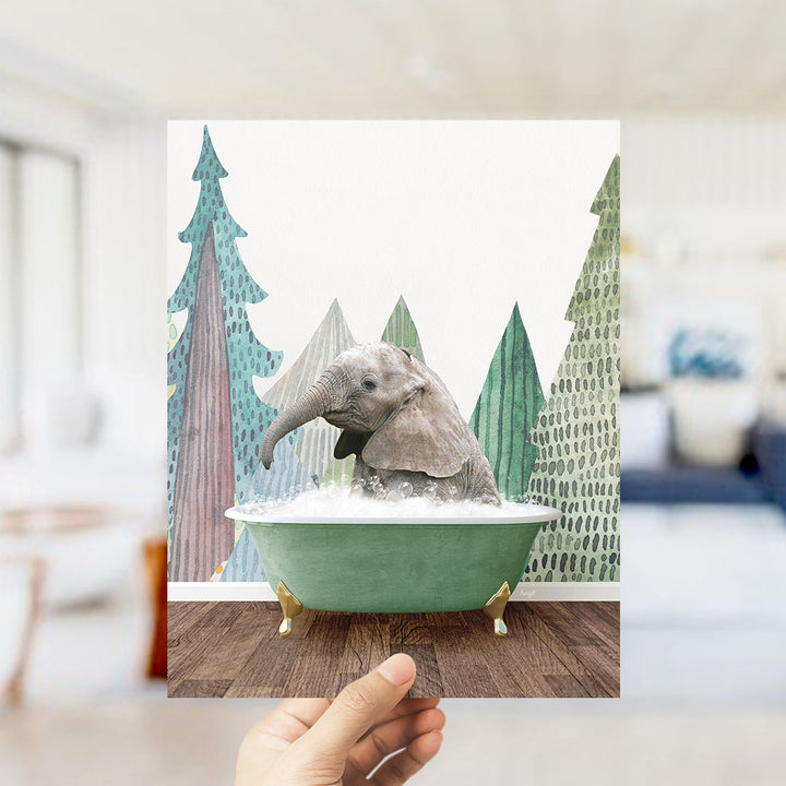 A hand holds up a framed image depicting a baby elephant sitting in a green bathtub, surrounded by a forest-themed background.