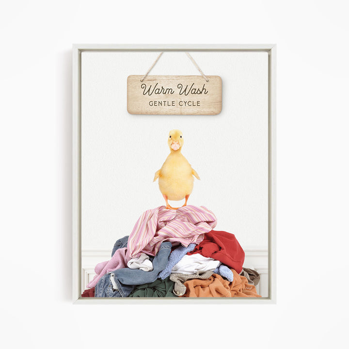 A yellow duck standing on a pile of clothes, with a wooden sign above that reads "Warm Wash Gentle Cycle".