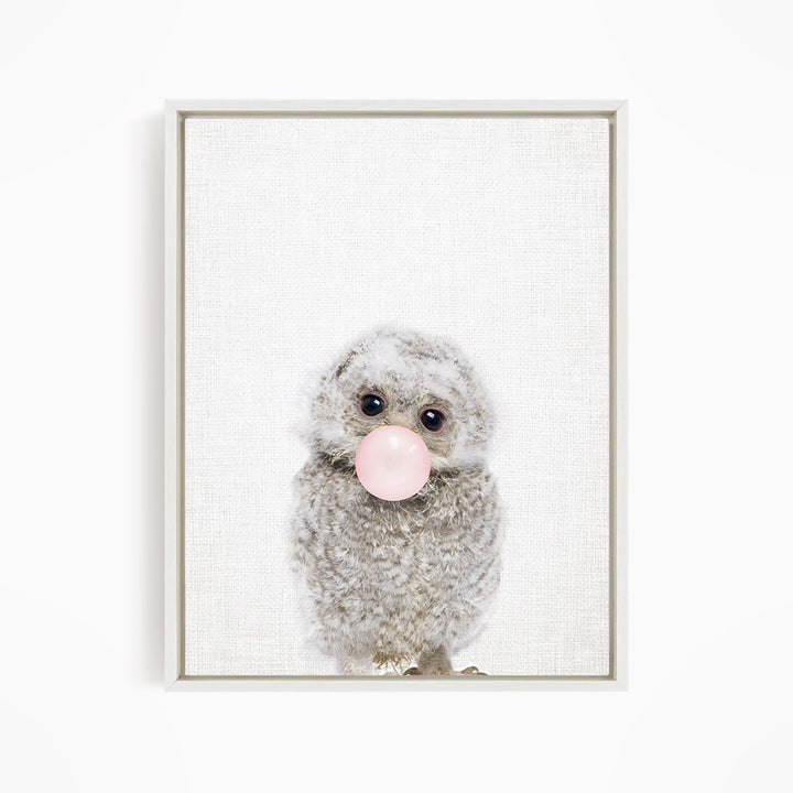 A fluffy gray owl with large eyes is blowing a pink bubblegum bubble.