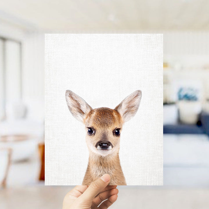A hand is holding up a white canvas print featuring a close-up portrait of a deer with large ears and a small nose.