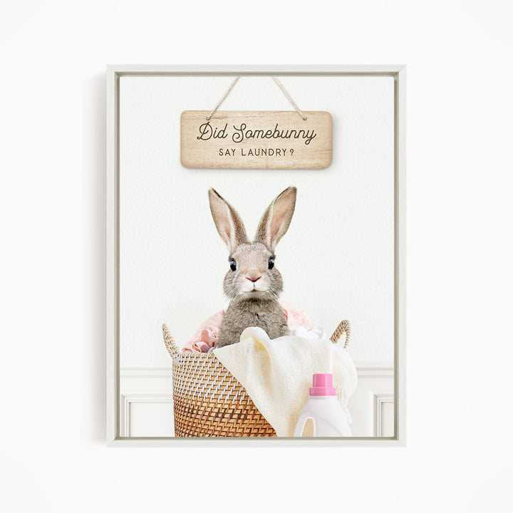 A cute rabbit sitting in a basket filled with laundry, with a sign above that says "Did Somebunny Sat Laundry?".