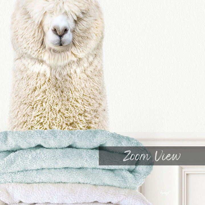 A fluffy white alpaca sits atop a stack of light blue towels, with a white wall in the background.