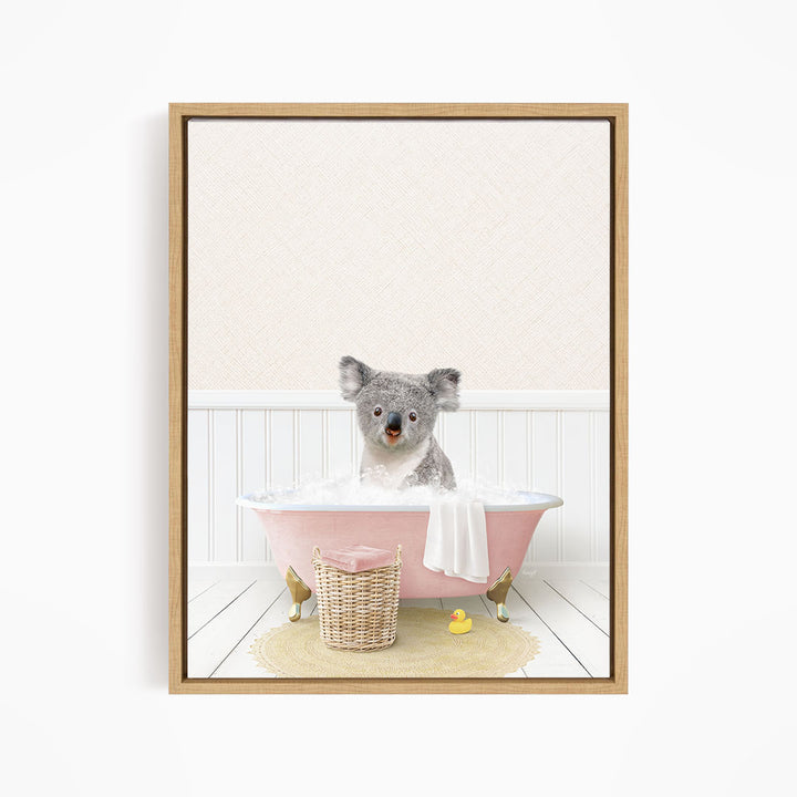 A koala bear sitting in a pink bathtub filled with water, surrounded by a yellow rubber duck and a wicker basket.