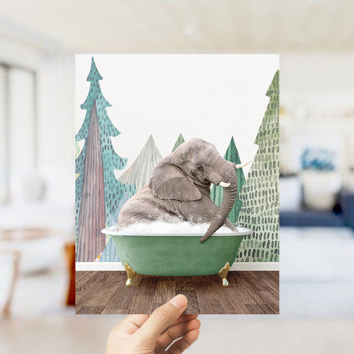A hand holds up a framed image depicting a gray elephant sitting in a green bathtub, surrounded by a forest-themed background.
