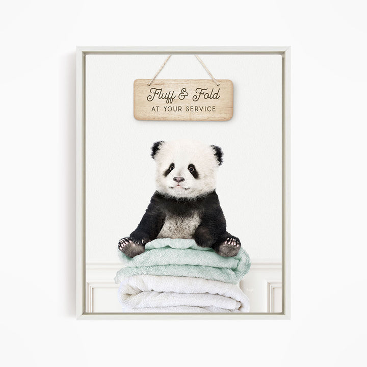 A panda bear sitting on a stack of towels, with a wooden sign above that says "Fuffy & Fold at your service".
