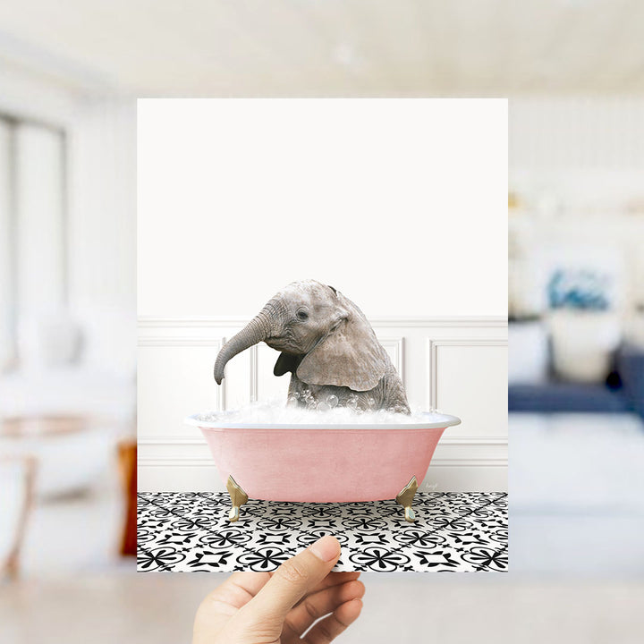 A small gray elephant is sitting in a pink bathtub filled with water, surrounded by a black and white patterned floor.
